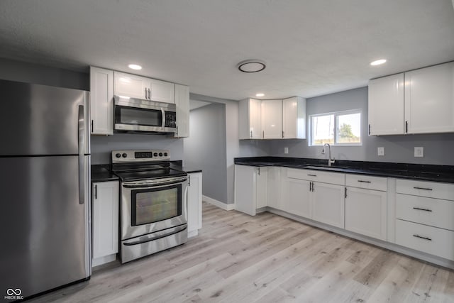 kitchen with a sink, stainless steel appliances, light wood-style floors, and white cabinets