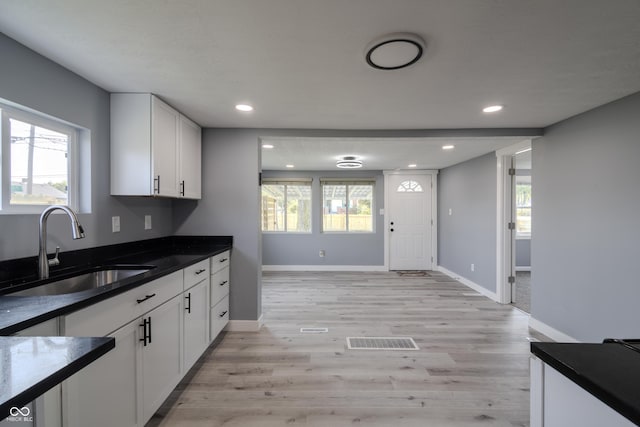 kitchen with light wood finished floors, visible vents, recessed lighting, white cabinets, and a sink