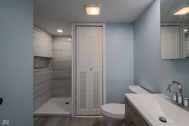 full bath with toilet, tiled shower, wood finished floors, a closet, and vanity