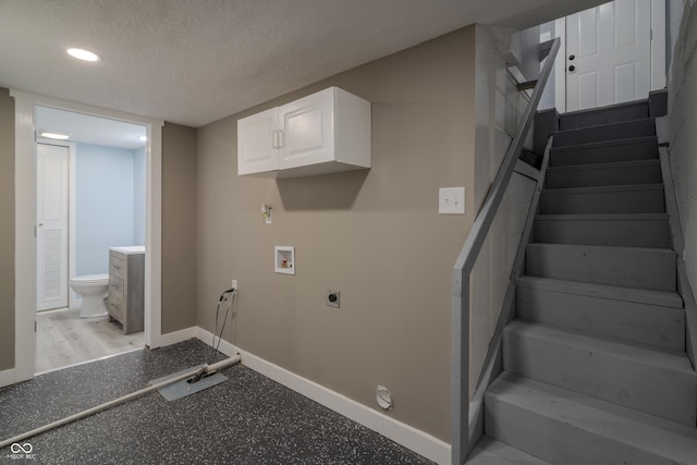 interior space featuring hookup for a washing machine, baseboards, hookup for an electric dryer, cabinet space, and a textured ceiling