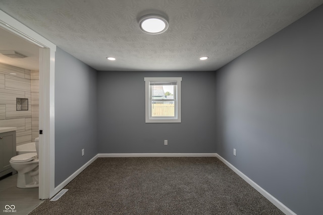 interior space featuring ensuite bath, carpet, baseboards, and a textured ceiling