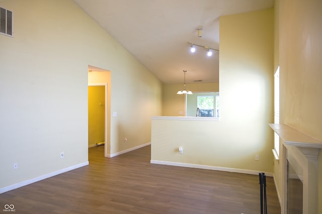 spare room featuring a chandelier, rail lighting, dark wood-type flooring, and high vaulted ceiling