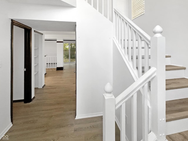 stairway with baseboards, wood finished floors, and a towering ceiling