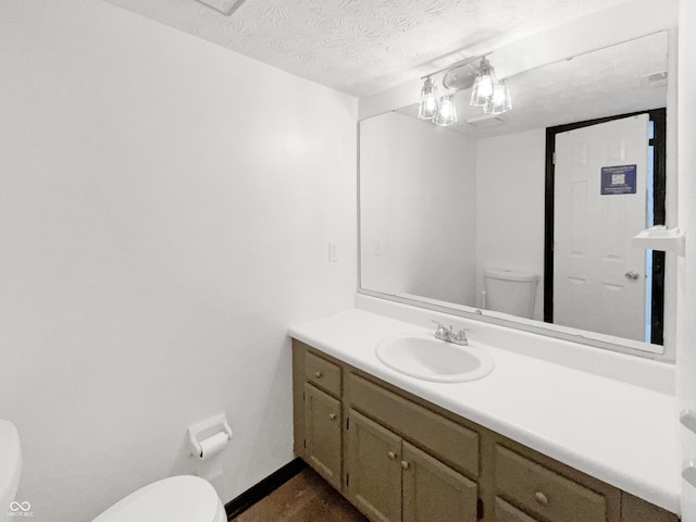 half bathroom featuring toilet, vanity, baseboards, and a textured ceiling