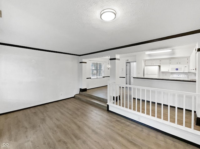 spare room with baseboards, wood finished floors, ornamental molding, and a textured ceiling