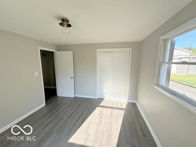 unfurnished bedroom with wood finished floors, baseboards, and a closet