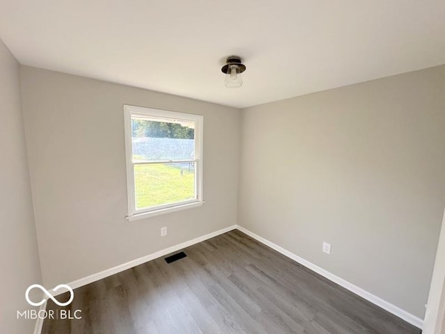 spare room with dark wood-style floors, visible vents, and baseboards