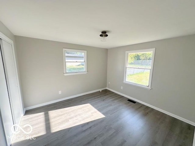 empty room featuring a wealth of natural light, visible vents, baseboards, and wood finished floors