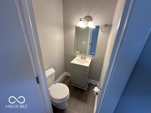 half bath featuring toilet, vanity, baseboards, and wood finished floors