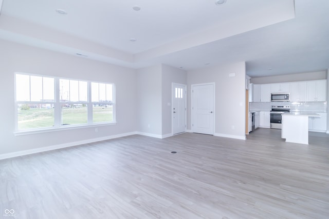 unfurnished living room with light wood-type flooring and a raised ceiling