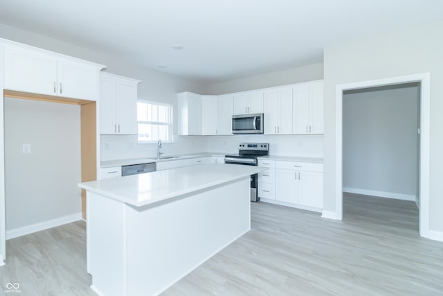 kitchen with stainless steel appliances, sink, light hardwood / wood-style flooring, white cabinets, and a kitchen island