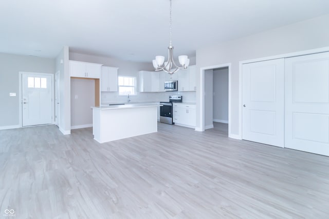 kitchen with appliances with stainless steel finishes, decorative light fixtures, a center island, light hardwood / wood-style floors, and white cabinetry