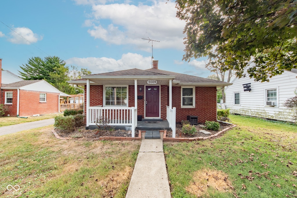 bungalow featuring covered porch, cooling unit, and a front yard