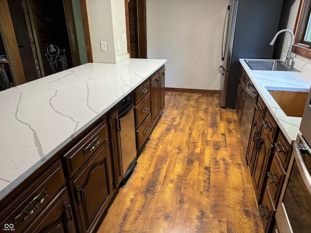 kitchen with dishwasher, dark wood-type flooring, light stone counters, and sink