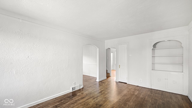 empty room featuring built in shelves and dark hardwood / wood-style floors