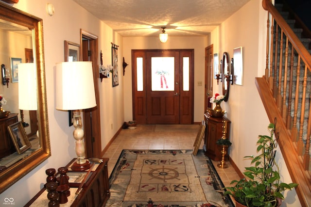 entryway with a textured ceiling, stairs, and baseboards