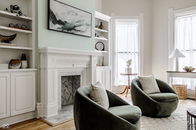 living room with a tiled fireplace, built in features, light hardwood / wood-style flooring, and a wealth of natural light