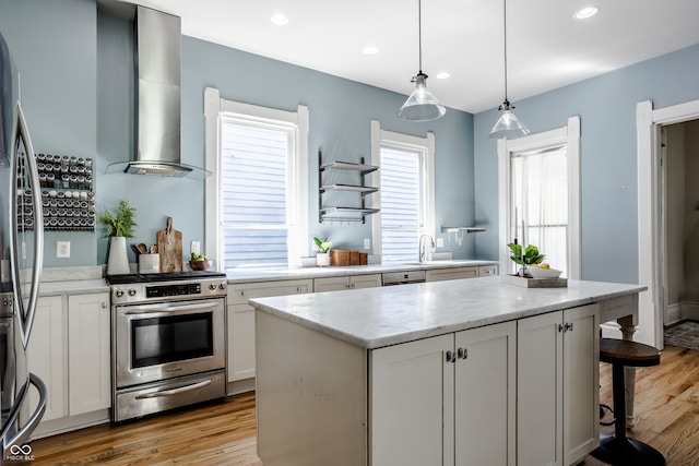 kitchen with a center island, wall chimney exhaust hood, stainless steel appliances, and light hardwood / wood-style floors