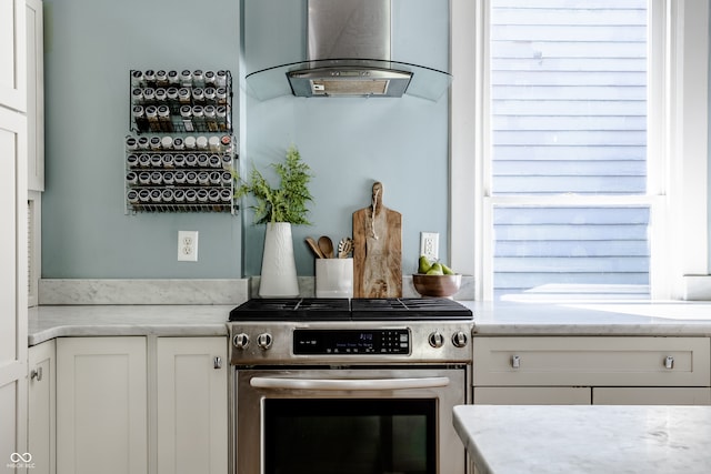 kitchen featuring island range hood, light stone counters, high end stove, and white cabinets