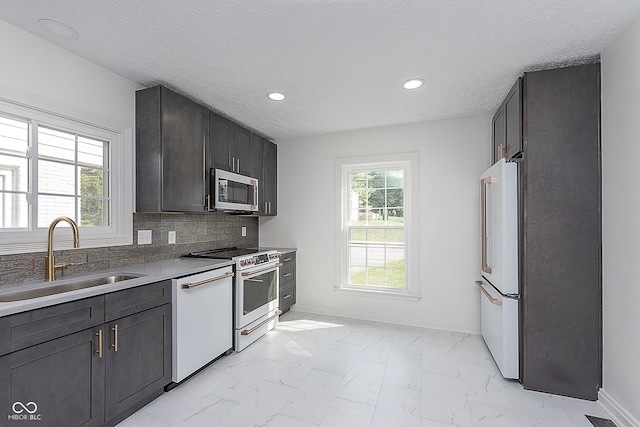 kitchen featuring a textured ceiling, sink, backsplash, and white appliances