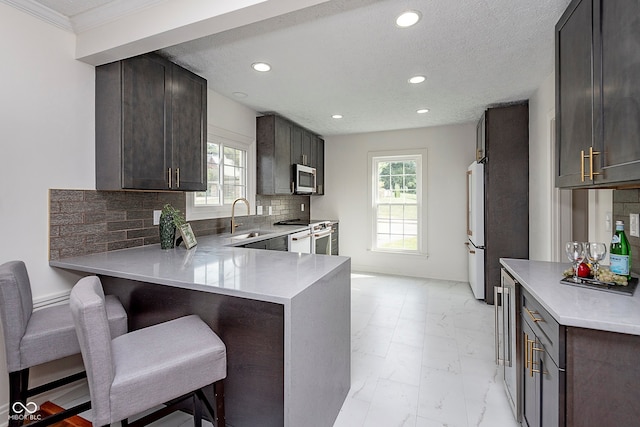 kitchen featuring kitchen peninsula, stainless steel appliances, a healthy amount of sunlight, sink, and a kitchen bar