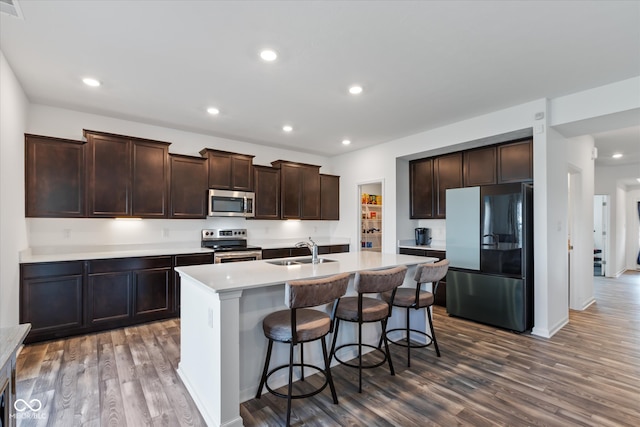 kitchen with hardwood / wood-style flooring, a kitchen island with sink, sink, a kitchen breakfast bar, and appliances with stainless steel finishes