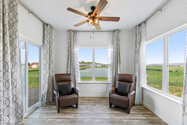 sitting room with a healthy amount of sunlight, a water view, ceiling fan, and light hardwood / wood-style flooring