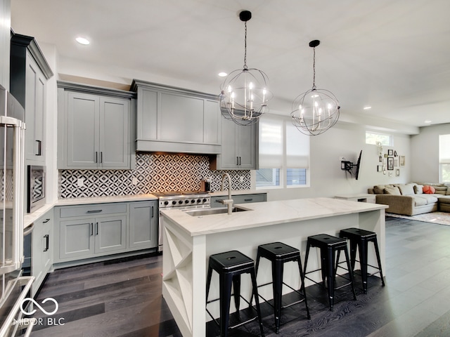 kitchen with an island with sink, a notable chandelier, dark hardwood / wood-style floors, and gray cabinets