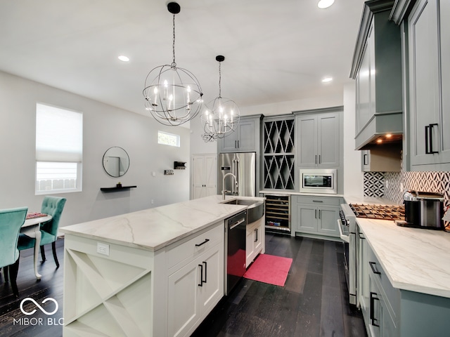 kitchen with high end appliances, a notable chandelier, dark hardwood / wood-style floors, pendant lighting, and a kitchen island with sink