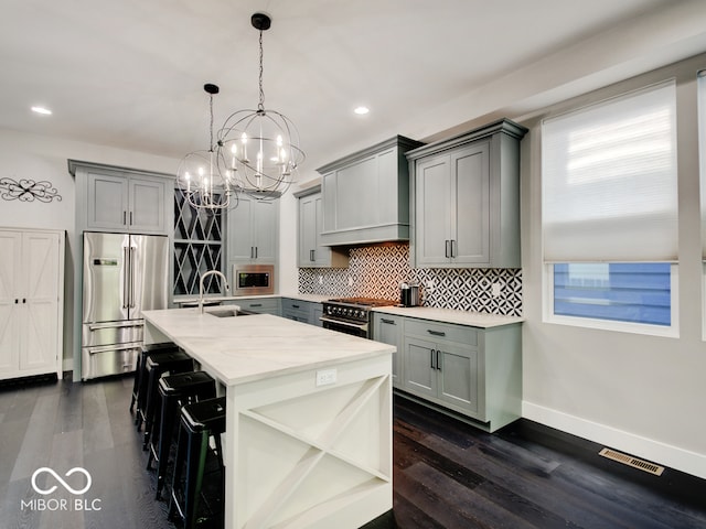 kitchen with high end appliances, an inviting chandelier, decorative light fixtures, a breakfast bar, and dark wood-type flooring