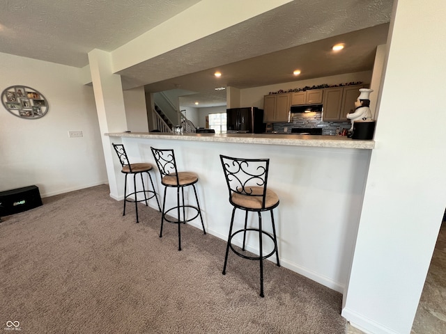 kitchen featuring a textured ceiling, a kitchen breakfast bar, kitchen peninsula, carpet flooring, and black fridge