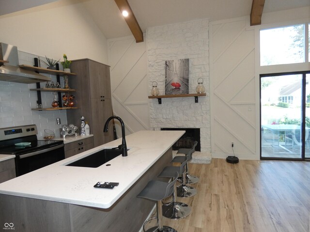 kitchen featuring stainless steel electric range, lofted ceiling with beams, light wood-type flooring, a breakfast bar area, and a center island with sink