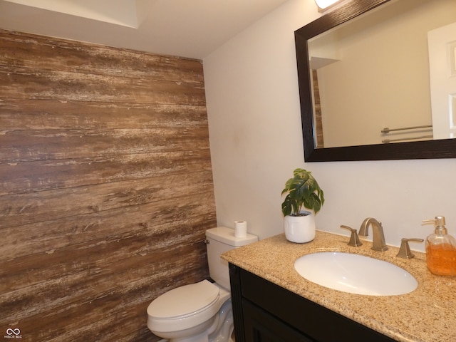 bathroom with toilet, wooden walls, and vanity