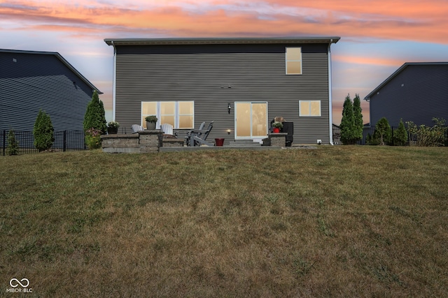 back house at dusk featuring a lawn and a patio