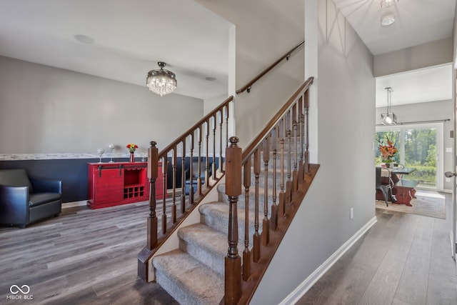 stairs with wood-type flooring and an inviting chandelier