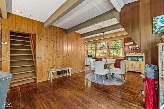 dining room featuring an inviting chandelier, beamed ceiling, wooden walls, and dark wood-type flooring