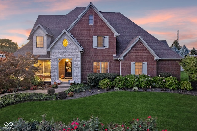 traditional-style house featuring brick siding, a shingled roof, a yard, and stone siding