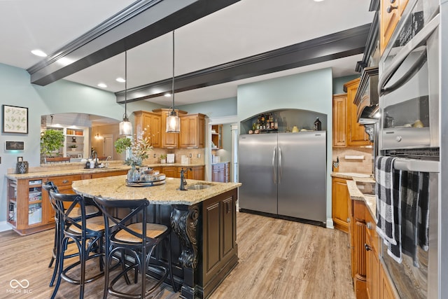 kitchen featuring light stone counters, a kitchen breakfast bar, backsplash, a center island with sink, and stainless steel fridge