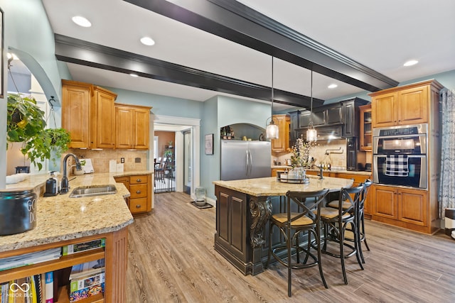 kitchen with light stone counters, backsplash, appliances with stainless steel finishes, a center island, and light hardwood / wood-style floors