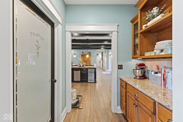 kitchen featuring light stone counters, light hardwood / wood-style flooring, hanging light fixtures, and stainless steel dishwasher