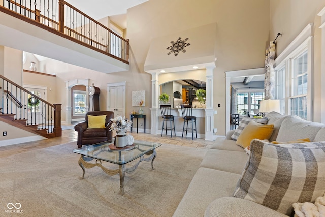 living room with light wood-type flooring, a towering ceiling, and ornate columns