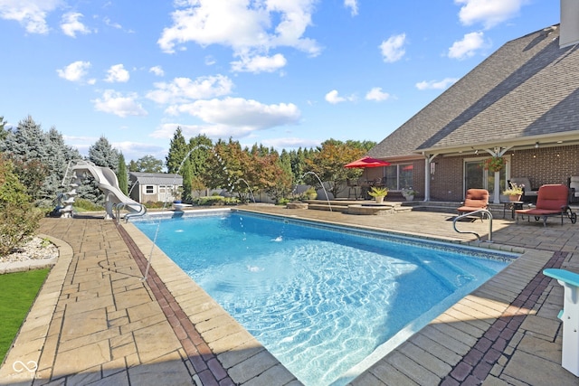 pool featuring an outdoor structure, a water slide, a patio, and a storage shed