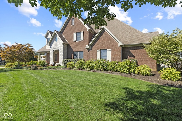 view of front of property featuring brick siding, a front yard, and roof with shingles