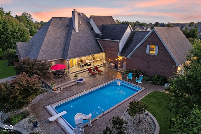 pool at dusk featuring an outdoor hangout area, an outdoor pool, a patio area, outdoor dining space, and a lawn
