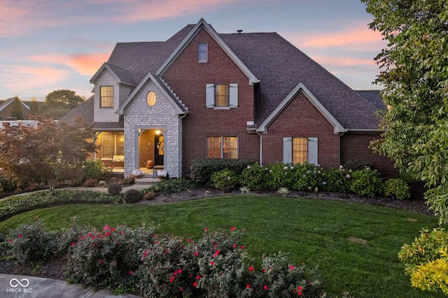 traditional-style home featuring a front yard, a shingled roof, brick siding, and stone siding