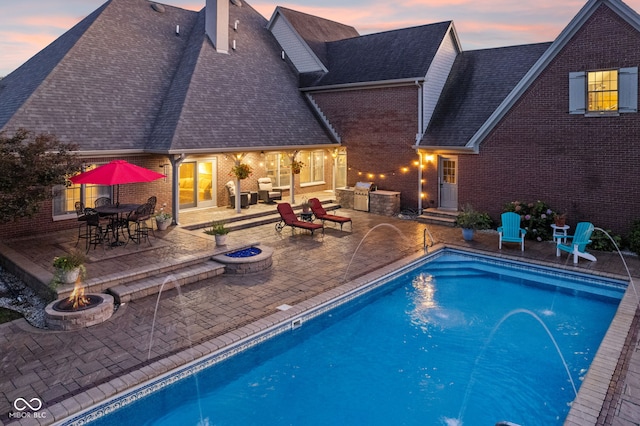 pool at dusk with pool water feature, a grill, a patio, and an outdoor fire pit