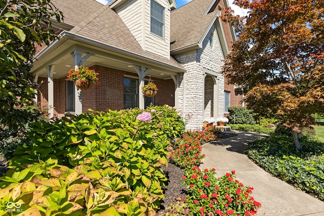 view of property exterior featuring a shingled roof, covered porch, and brick siding
