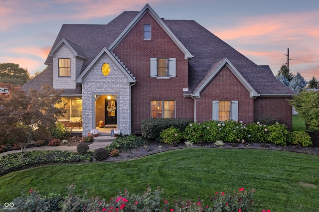 traditional home featuring roof with shingles, a front yard, brick siding, and stone siding