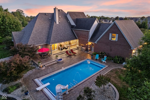 pool at dusk with a diving board and a patio area