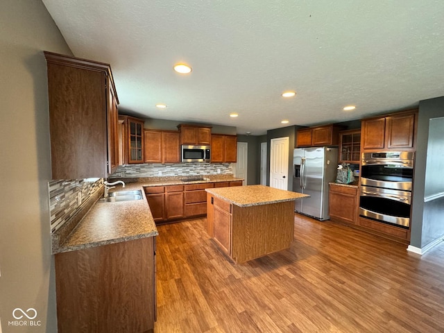 kitchen featuring sink, backsplash, hardwood / wood-style flooring, appliances with stainless steel finishes, and a center island